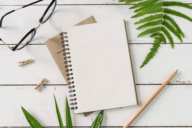 istock Blank notebook with green leaves on white wooden table 873559036