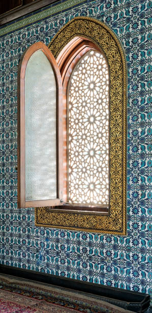 istock Wooden arched window framed by golden floral pattern ornaments over ceramic tiles wall with floral blue patterns 873567096