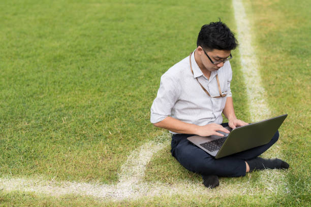 business-mann sitzt arbeit mit computer-laptop auf fußballplatz. arbeitskonzept. kopieren sie raum für konzeptionelle nachricht. - soccer field soccer single line field stock-fotos und bilder