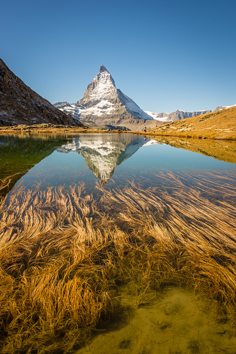 The iconic Matterhorn peak reflected in the clear and flat water of Riffelsee above the tourist town of Zermatt, Switzerland.