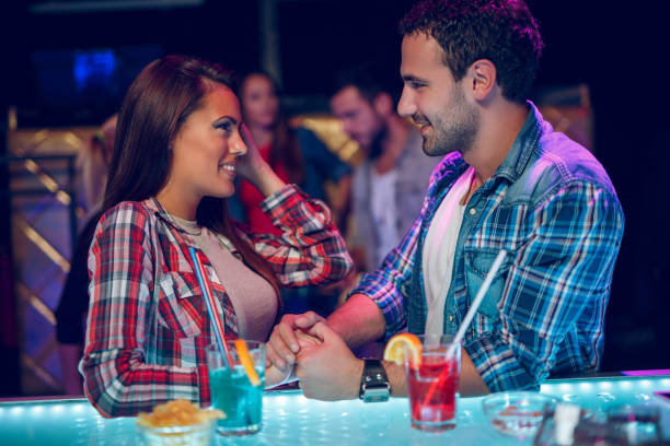 jovem casal feliz flertando com uma bebida na boate - drinking couple bar counter bar - fotografias e filmes do acervo