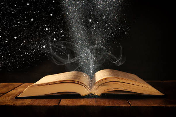 istock image of open antique book on wooden table with glitter overlay. 873594652