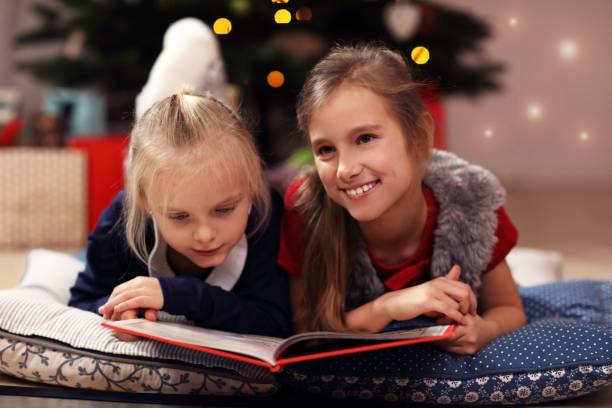 istock Two cute little sisters reading story book together under Christmas tree 873600562