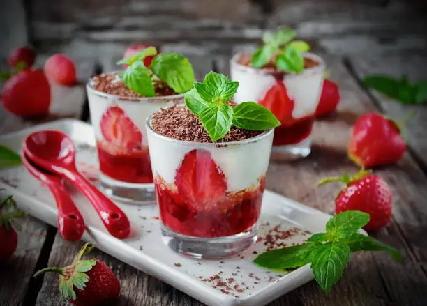 Italian dessert tiramisu with fresh strawberries and chocolate in portion glasses on a wooden background