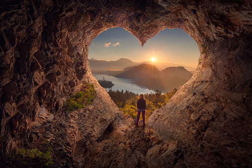 Mujer joven en la cueva de la forma del corazón hacia el amanecer idílico photo