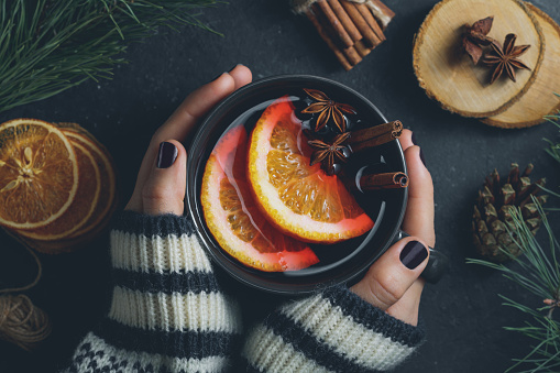 Top view of the girl's hands in a winter sweater are holding a big black cup with hot mulled wine. The concept of cozy winter Holidays.