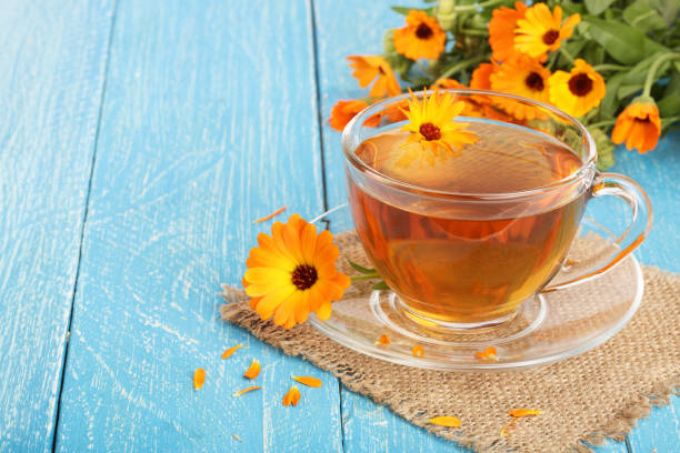 istock Calendula tea with fresh flowers on blue wooden background 873647198