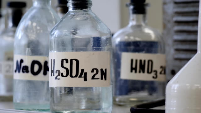 Bottles of solutions stored on shelf in laboratory. Bottles with chemical solutions of NaOH, H2so4 and HNO3. Sulfuric acid, sodium hydroxide, nitric acid
