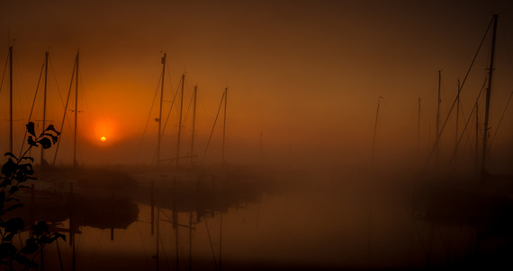 A small harbor covered in mist around sunrise with sailboats