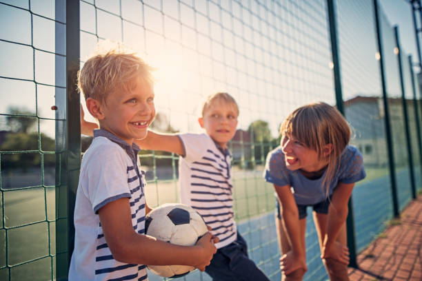 Kids having fun at the schoolyard Kids laughing and having fun during the schools break. Kids are standing at the schoolyard. One of the boys is holding a soccer ball.
 recess soccer stock pictures, royalty-free photos & images