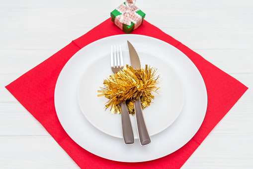 A knife and fork in white plate on red napkin decorated with a Christmas wreath on white table top view