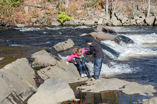 Boy helping his sister walking on rocks over  St-Charles river in Quebec city during day of autumn