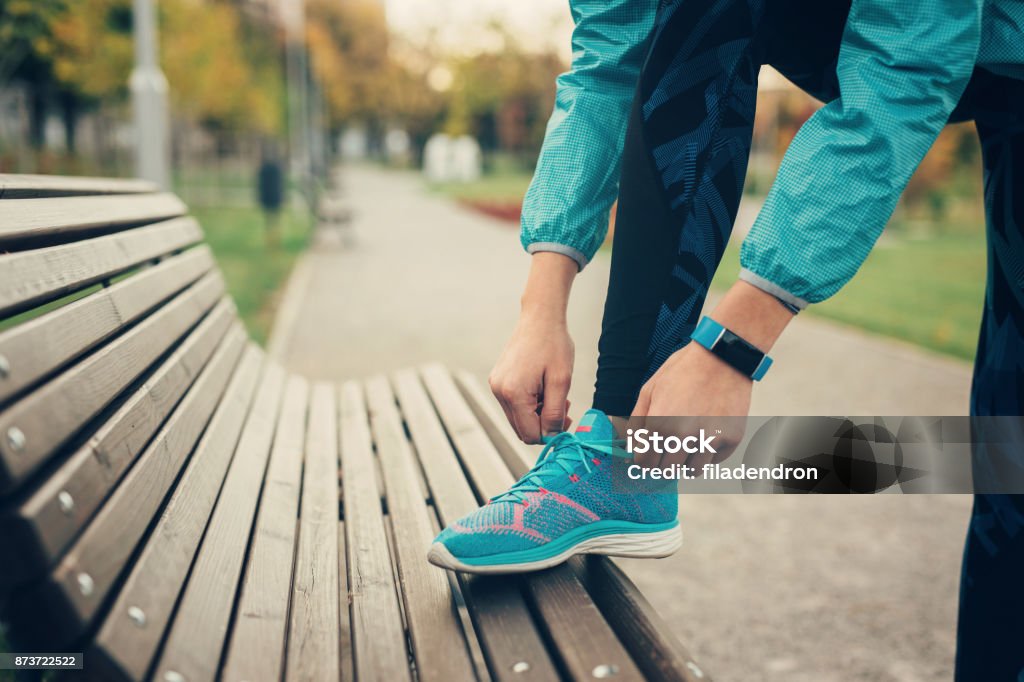 Woman tying up her shoe lace Woman tying up her shoe lace on a bench in the park. Running Stock Photo