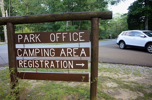 Close up of park office camping area registration road arrow sign with passing car in public state park.