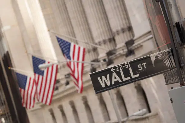 Wall Street sign with the blurred flags of the stock exchange as background. October 2017