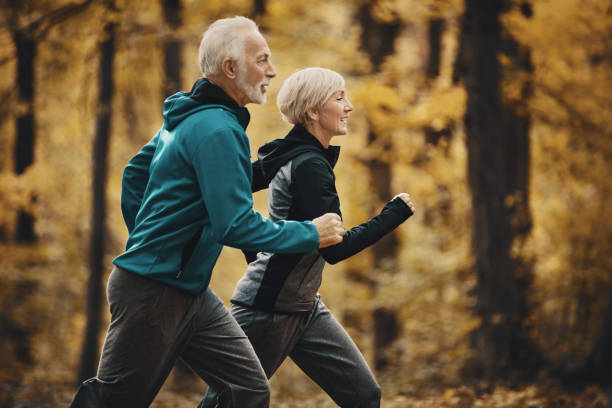 старшая пара бег трусцой в лесу. - senior adult running jogging senior women стоковые фото и изображения