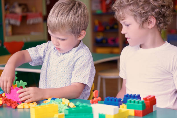 istock Cute caucasian boy in a white shirt playing with colorful constructor details. Activities with children in kindergarten. 873746668