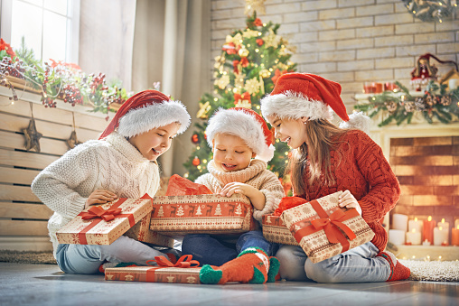 Merry Christmas and Happy Holidays! Cheerful cute children opening gifts. Kids having fun near tree in the morning. Loving family with presents in room.
