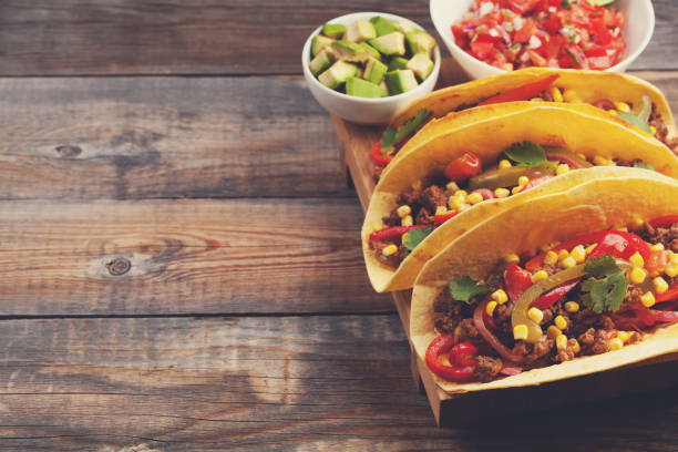 istock Three Mexican tacos with minced beef and mix vegetables on old rustic table. Mexican dish with sauce salsa in bowl and avocado. Spicy and hot street food. with copy space 873755062