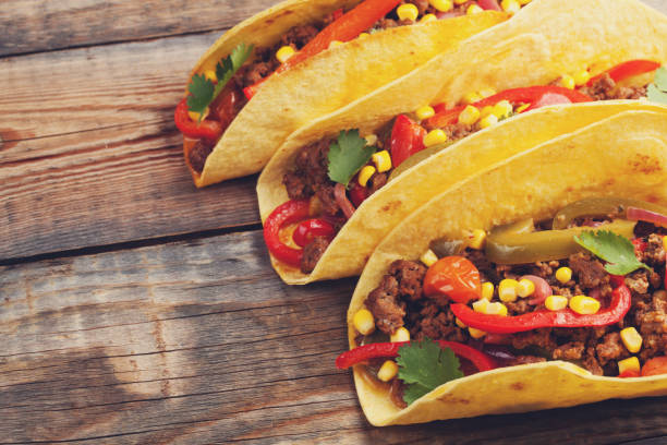 istock Three Mexican tacos with minced beef and mix vegetables on old rustic table. Mexican dish with sauce salsa in bowl and avocado. Spicy and hot street food. with copy space 873755092