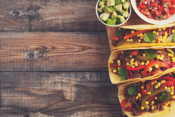 istock Three Mexican tacos with minced beef and mix vegetables on old rustic table. Mexican dish with sauce salsa in bowl and avocado. Spicy and hot street food. Top view with copy space 873755094