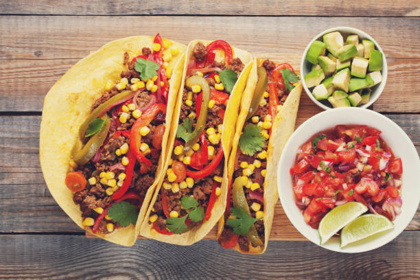 istock Three Mexican tacos with minced beef and mix vegetables on old rustic table. Mexican dish with sauce salsa in bowl and avocado. Spicy and hot street food. Top view 873755098