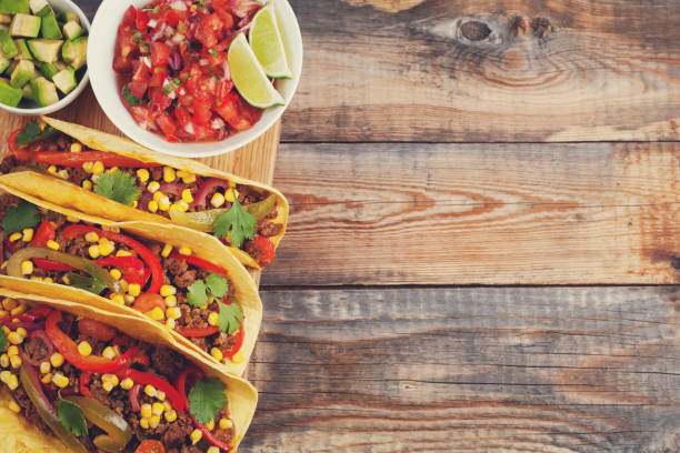 istock Three Mexican tacos with minced beef and mix vegetables on old rustic table. Mexican dish with sauce salsa in bowl and avocado. Spicy and hot street food. Top view with copy space 873755110