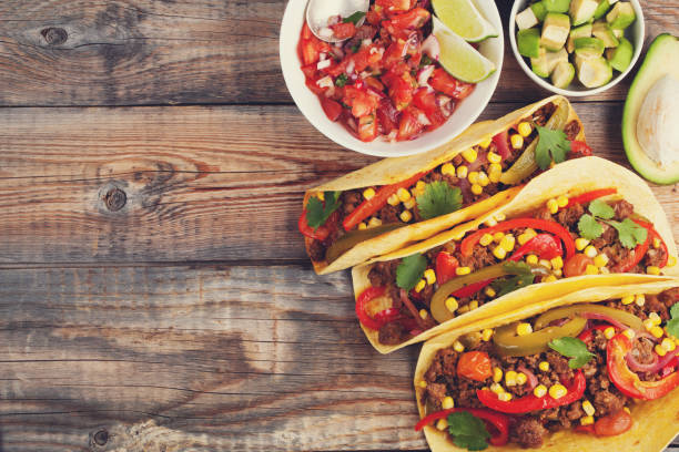 istock Three Mexican tacos with minced beef and mix vegetables on old rustic table. Mexican dish with sauce salsa in bowl and avocado. Spicy and hot street food. Top view with copy space 873755120