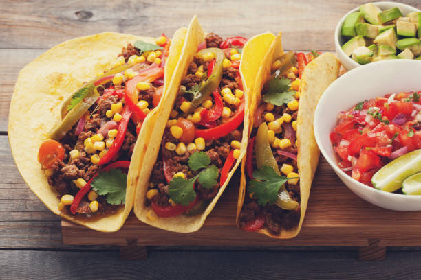 istock Three Mexican tacos with minced beef and mix vegetables on old rustic table. Mexican dish with sauce salsa in bowl and avocado. Spicy and hot street food. Close-up 873755124