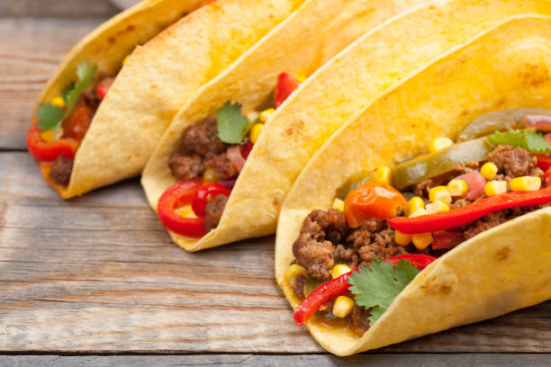 istock Three Mexican tacos with minced beef and mix vegetables on old rustic table. Mexican dish with sauce salsa in bowl and avocado. Spicy and hot street food. Close-up 873755126