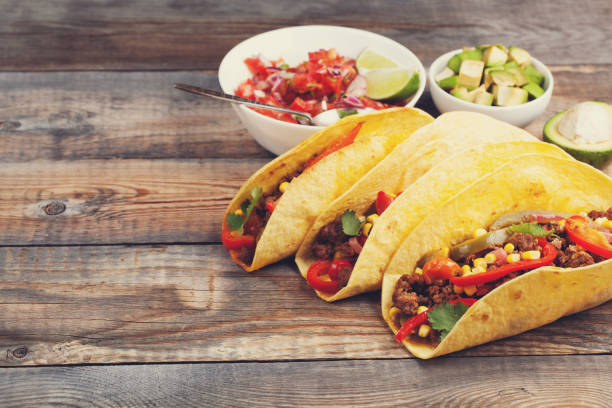 istock Three Mexican tacos with minced beef and mix vegetables on old rustic table. Mexican dish with sauce salsa in bowl and avocado. Spicy and hot street food. with copy space 873755128