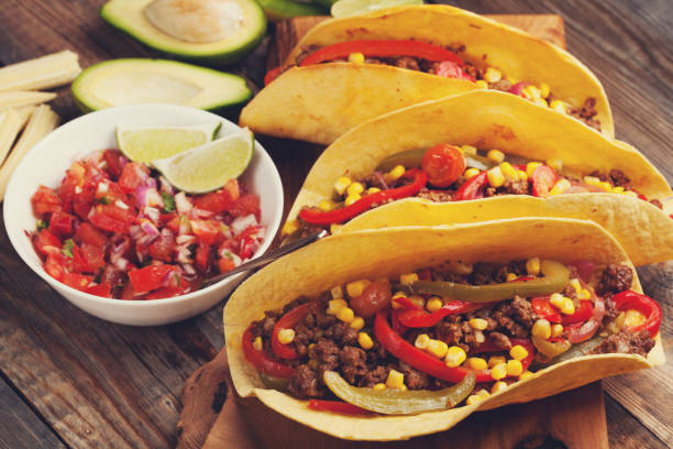 istock Three Mexican tacos with minced beef and mix vegetables on old rustic table. Mexican dish with sauce salsa in bowl and avocado. Spicy and hot street food. Close-up 873755132