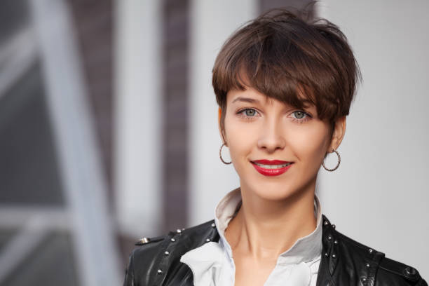 Happy young fashion woman in leather jacket walking in city street stock photo