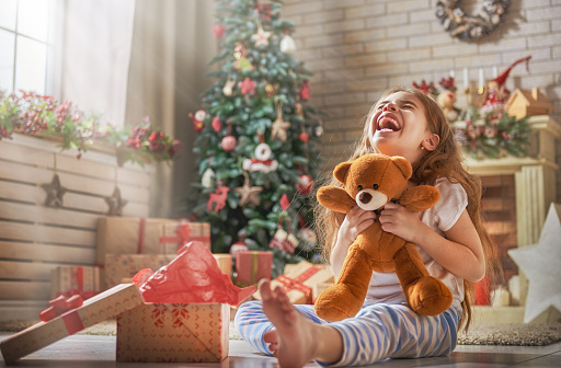 Happy holidays! Cute little child opening present near Christmas tree. The girl laughing and enjoying the gift.