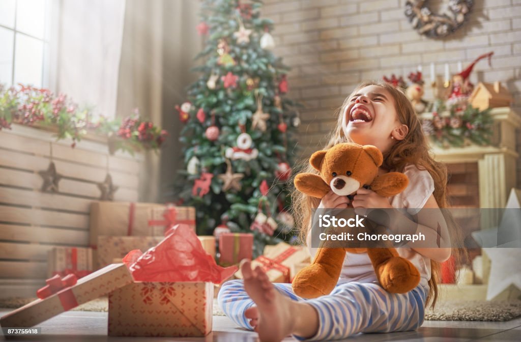 child opening present Happy holidays! Cute little child opening present near Christmas tree. The girl laughing and enjoying the gift. Child Stock Photo