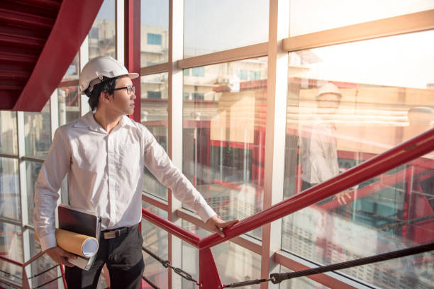 istock Young Asian Engineer or Architect holding files and architectural drawing at construction site 873761456