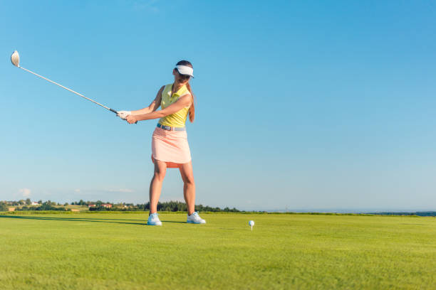 istock Professional female golf player smiling while swinging a driver club before hitting the ball 873762148