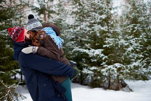 Having fun in winter park: loving young couple gently embracing and kissing each other while spending weekend outdoors