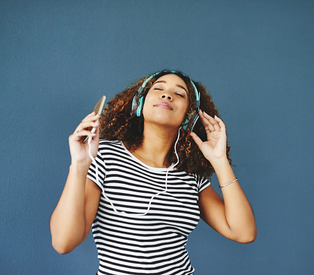 Studio shot of an attractive young woman listening to music on her cellphone