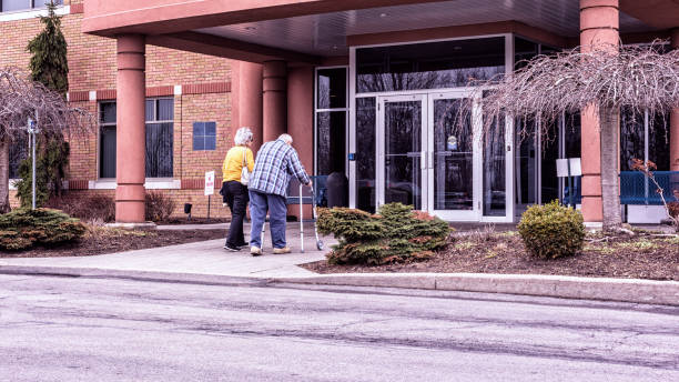 Elderly Man Using Walker Entering Medical Office With Daughter An elderly senior adult man using an orthopedic medical equipment walker to support himself as he walks is entering a medical office building near Rochester, New York State, USA. His senior adult woman home caregiver daughter is accompanying him to help with his doctor's appointment. revised stock pictures, royalty-free photos & images