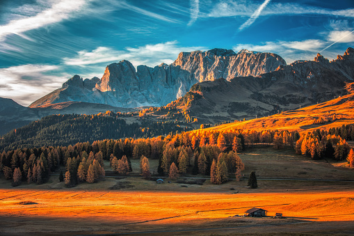 Aerial autumn sunrise scenery with yellow larches and small alpine building and Odle - Geisler mountain group on background. Alpe di Siusi (Seiser Alm), Dolomite Alps, Italy