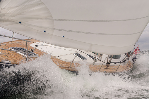 Close up of sailing boat, sail boat or yacht crashing through waves in a rough sea