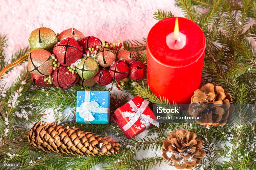 Christmas or New Year card. Burning red candle, cones, giftboxes, toys on fir tree branches and snow. Close up image Christmas or New Year card. Burning red candle, cones, giftboxes, toys on fir tree branches and snow. Close up image. Backgrounds Stock Photo