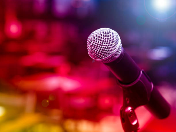 istock Electrical microphone stand on the stage with red, yellow, purple and blue light background 873814158