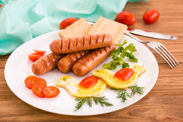 Ready breakfast. Fried sausages, scrambled eggs, tomatoes and greens. Wooden table