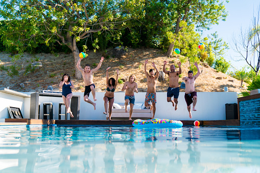 Group of friends jumping into a swimming pool on a summer day. Los Angeles, America. July 2017