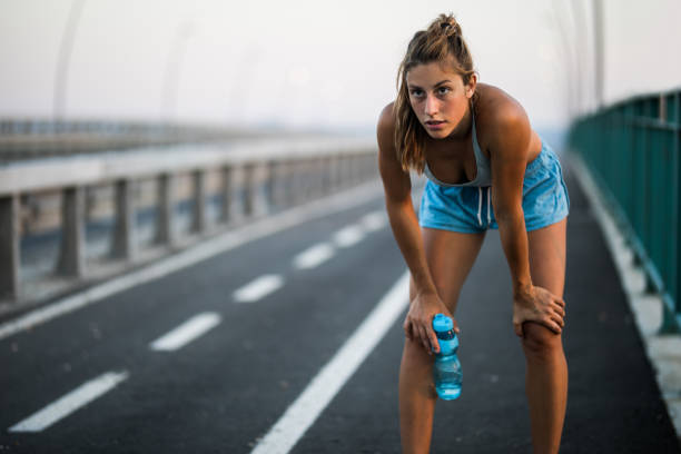 Exhausted athlete taking a water break from sports training outdoors. Young tired woman having a water break on the street. Copy space. groyne stock pictures, royalty-free photos & images