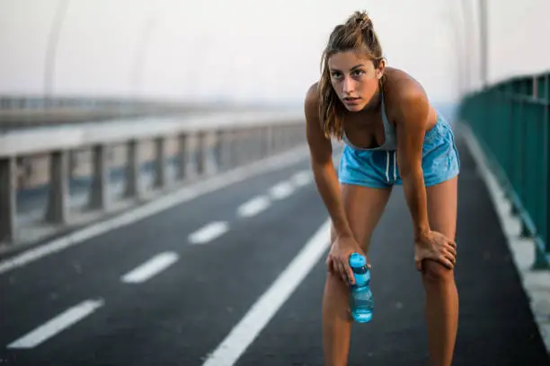 Young tired woman having a water break on the street. Copy space.