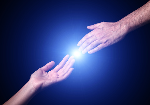 Reaching and touching hands. Bright light star flare with touching fingertips. Concept for salvation, rescue, friendship, guidance. Black background.