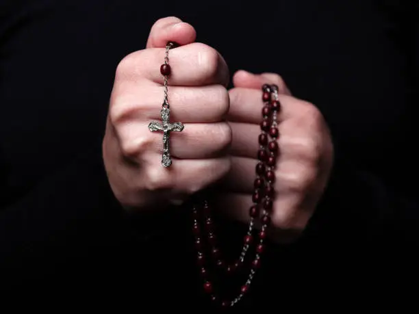 Female hands praying holding a rosary with Jesus Christ in the cross or Crucifix on black background. Woman with Christian Catholic religious faith